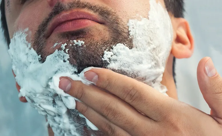 mężczyzna aklikujący piankę do golenia na twarz